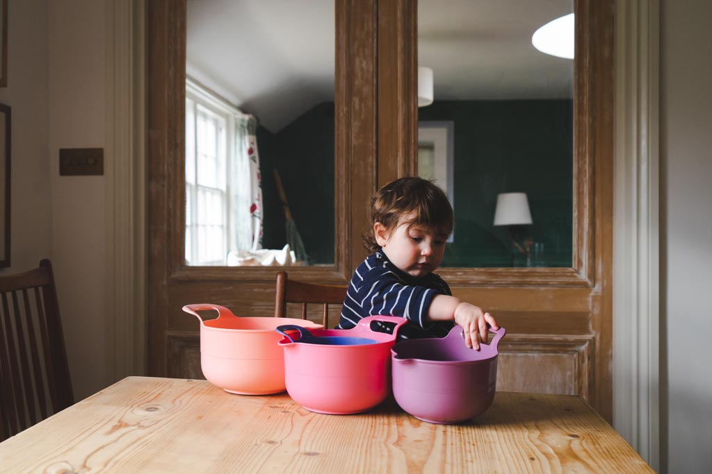 A toddler at a kitchen table, reaching into a row of three nesting bowls
