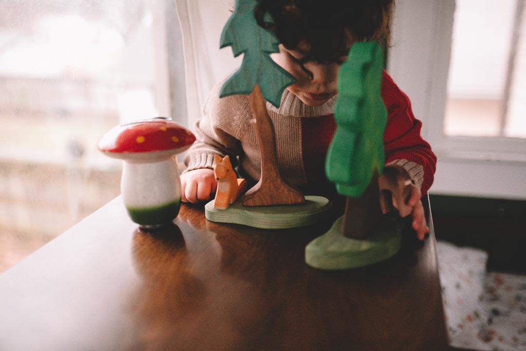 A child bent over a wooden fox, tree and toadstool on a polished table